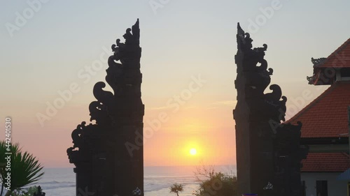 A beautiful bright tropical sunset through the Balinese religious divine gates. Explore Bali culture and architecture. Black silhouette of Candi Bentar on the beach entrance. Duality of Bali Hinduism. photo