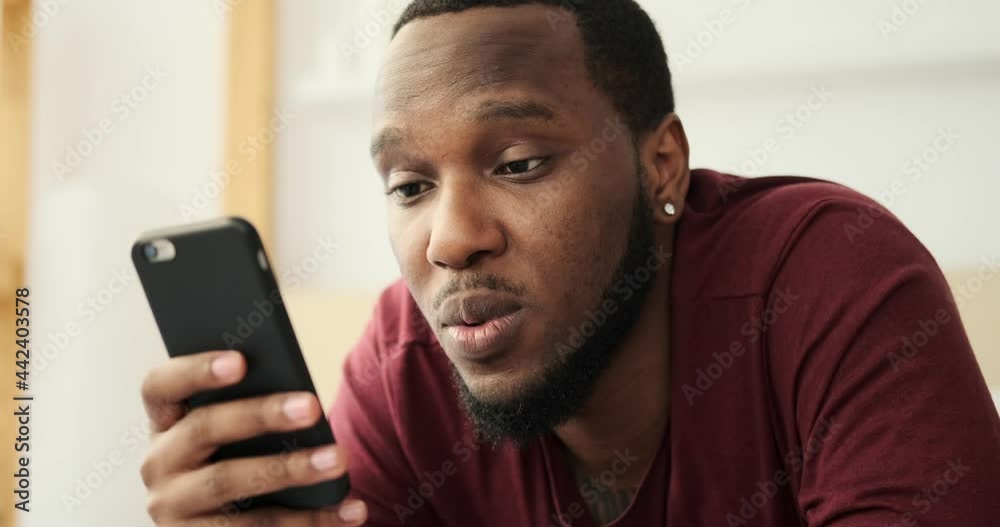 African American man text messaging using mobile phone at home