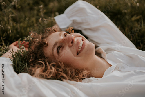 young happy, smiling woman with curls is lying in the grass enjoying spring