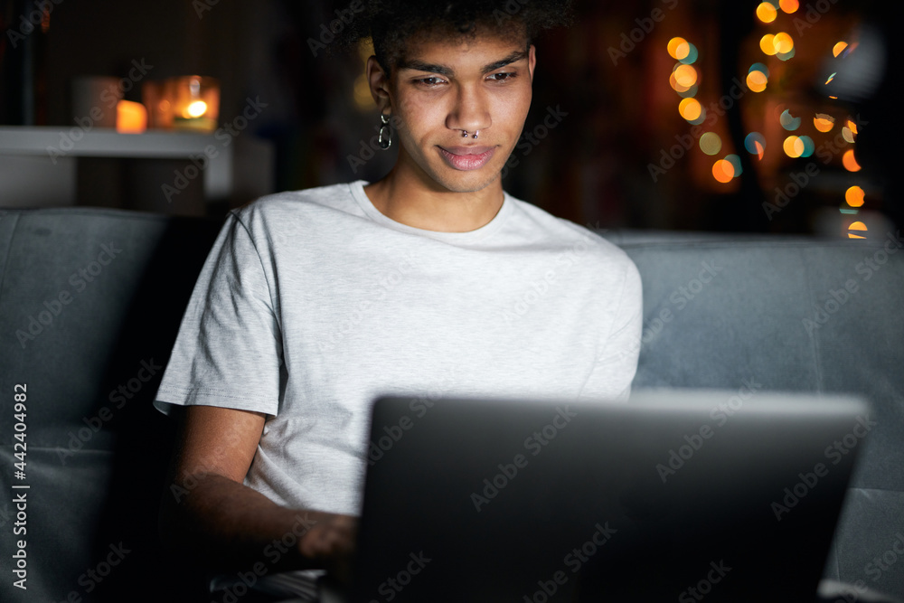 Entertainement. Night portrait of attractive young guy looking at the screen, watching videos, using laptop in dark room, sitting on a couch at home alone Entertainement. Night portrait of attractive young guy looking at the screen, watching videos, using laptop in dark room, sitting on a couch at home alone