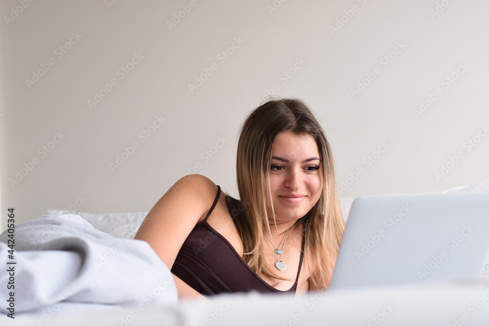 Young teenage girl laying on bed using laptop computer Young teenage girl laying on bed using laptop computer