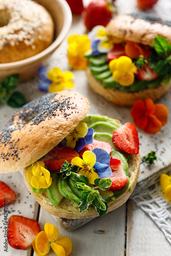 Bagel sandwich with addition avocado slices and edible pansy flowers, close up view. Delicious and beautiful vegan food