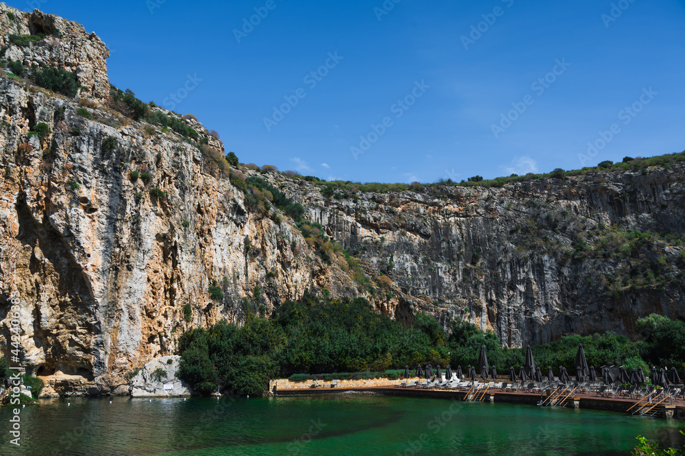 Vouliagmeni lake in Greece at sunny summer day. Small brackish-water lake fed. Scenic landscape of white mountain and green water. Thermal spring. SPA.