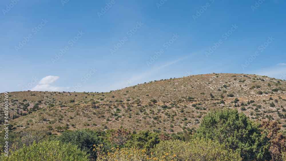 Scenic landscape of mountainous arid area. Hot sunny summer day. Southern nature. Dry grass. Green trees and bushes on hill.