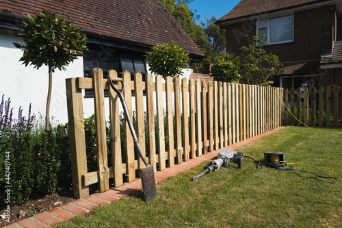 The installation of a wooden, natural wood colour, picket fence in a residential garden.