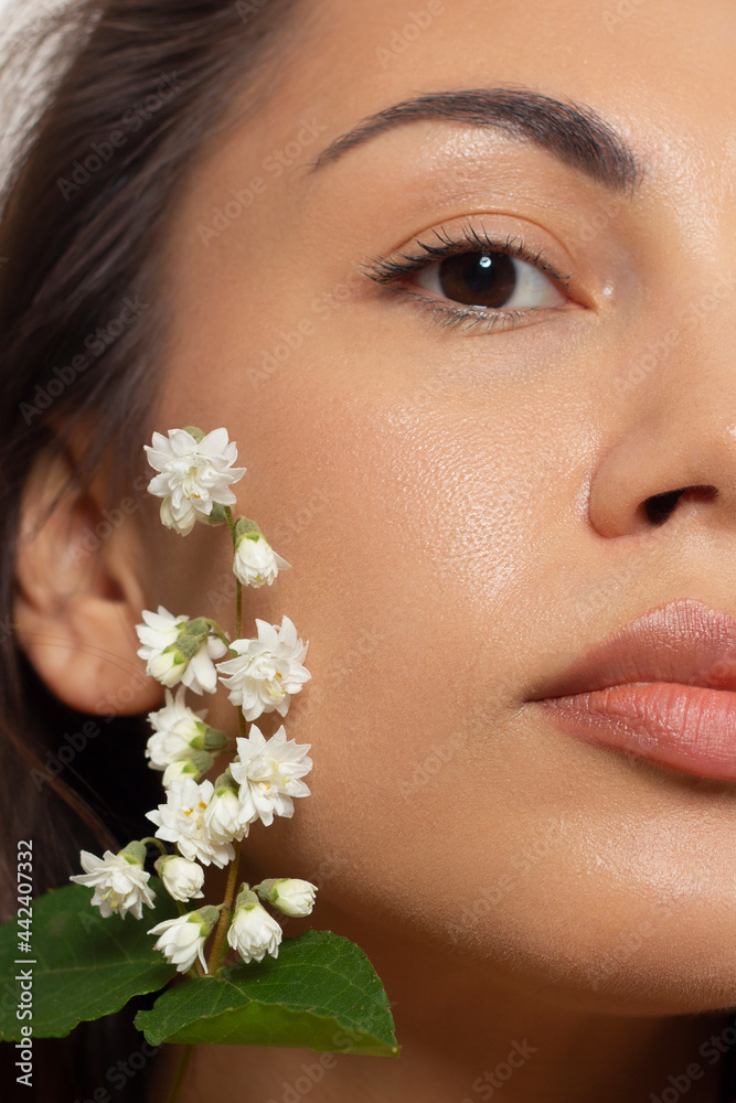Close up portrait of a face with beautiful skin and nude makeup, eyeliner and long eyelashes, puffy natural lips and white flowers. Fashion photography. Cosmetology and spa. Freshness of spring Close up portrait of a face with beautiful skin and nude makeup, eyeliner and long eyelashes, puffy natural lips and white flowers. Fashion photography. Cosmetology and spa. Freshness of spring