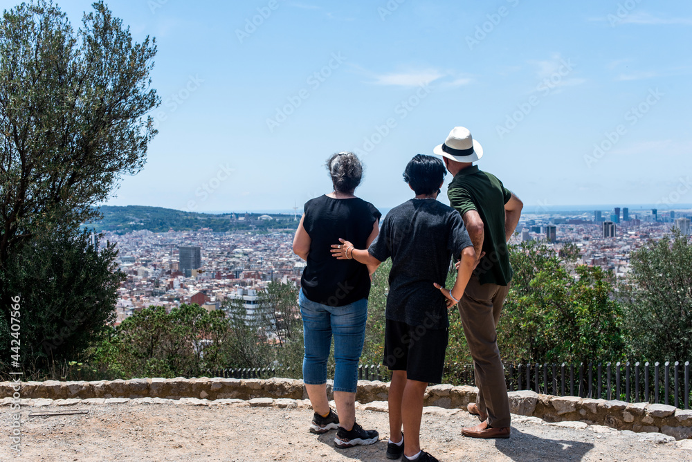 Una familia de tres turistas contemplando las vistas de una ciudad en verano desde un mirador. Barcelona ciudad desde lo alto de una colina.