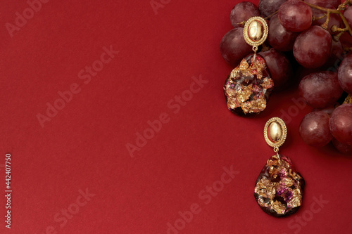 Studio shot of epoxy resin earrings with golden foil inside with a bunch of grapes isolated over red background