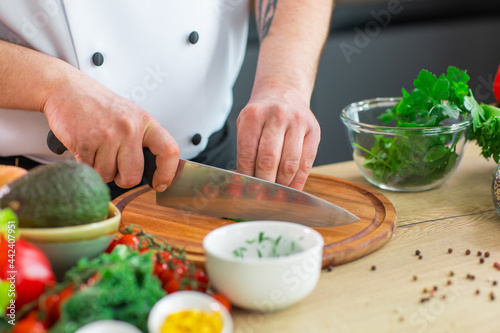 Young chef is cutting herbs and parsley in a modern kitchen. The man prepares food at home. Cooking healthy and tasty food.