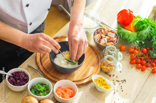 Young prepares a poke bowl in a modern kitchen. The man prepares food at home. Cooking healthy and tasty food. photo