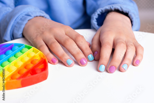 Little girl hands with beautiful manicure nails near toy, pop it