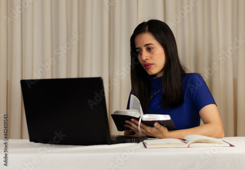 Woman in front of the computer writing, reading. with books, agenda, pencil, in virtual class, in virtual church, Woman, young man at desk. student. Teacher, with the bible. looking in the bible.