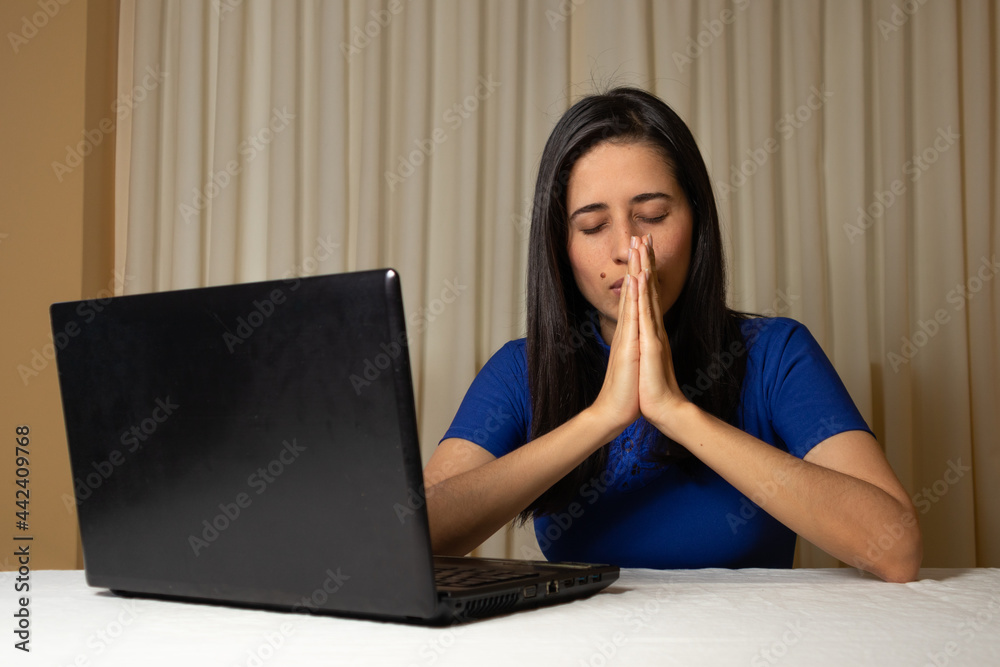 Christian and religious woman in front of the computer. virtual worship, virtual mass, virtual congregation. Woman praying in front of her laptop. faith. religious work.