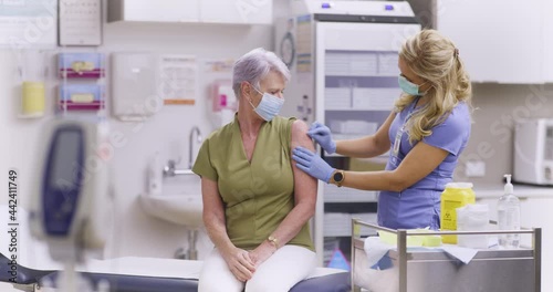A Wide Shot Of An American Female Medical Nurse Administering A Covid-19, SARS-CoV-2 Vaccine Injection With A Needle and Syringe, To An Elderly Woman. Wearing Safety Gloves And Protective Mask
