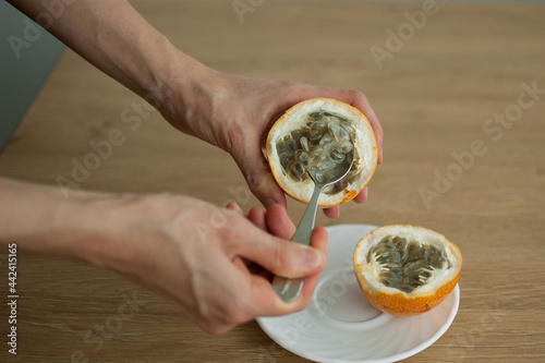 Female eats fresh organic ripe granadilla or yellow passion fruit with a spoon. Exotic fruits, healthy eating concept photo