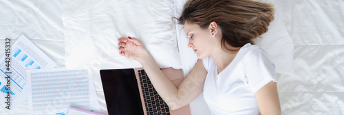 Woman sleeping in bed with laptop and documents top view