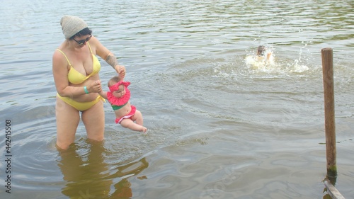 Canvas-taulu Mom with children in the water of a city lake, beach season in the suburbs