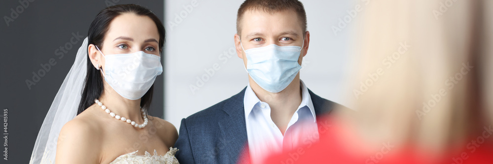 Bride and groom wearing medical protective masks standing in front of receptionist Bride and groom wearing medical protective masks standing in front of receptionist