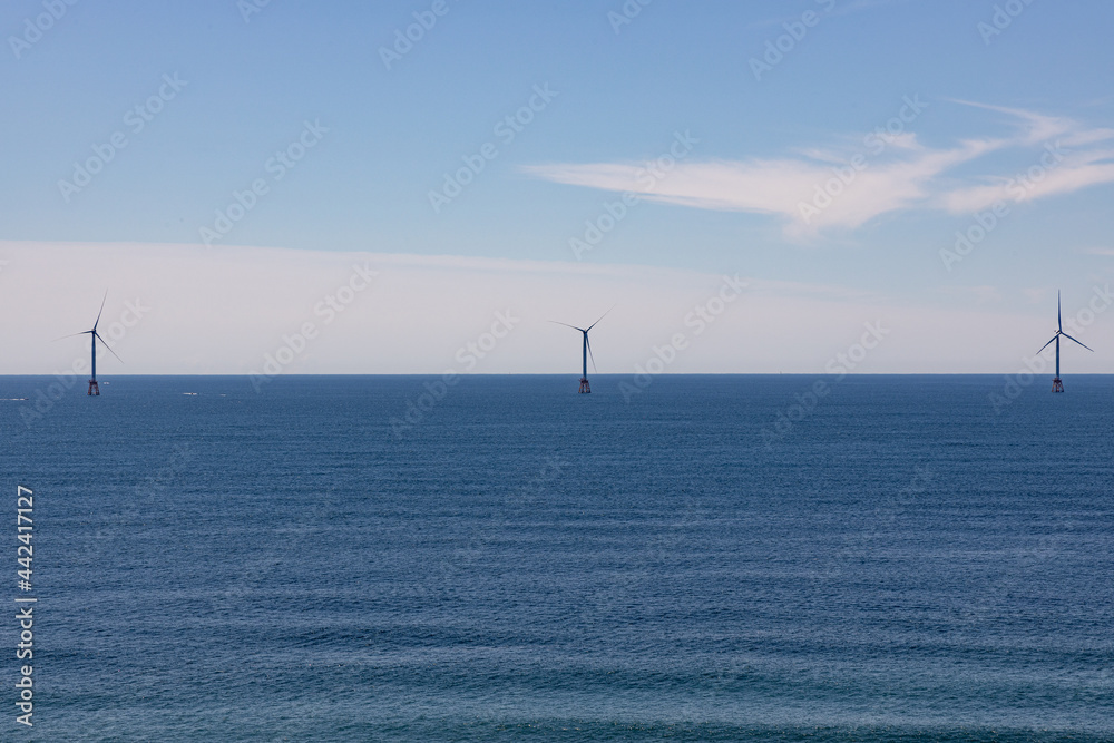 Three wind turbines out on the horizon and on a calm ocean