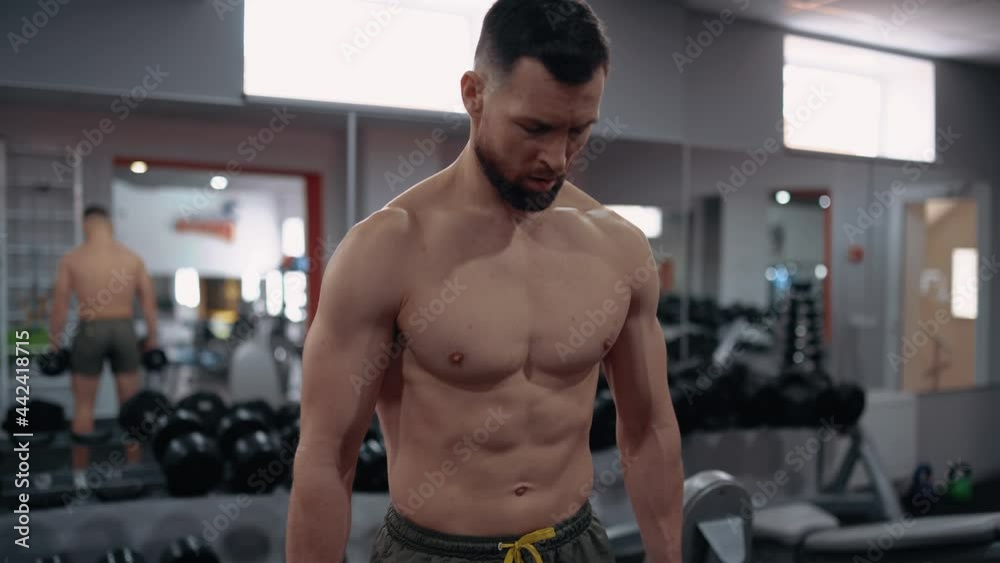 The sporty man, trained, sits with dumbbells in his hand, prepares for the next exercise, in a gym. Intense masculine energy. Healthy lifestyle. Sport concept The sporty man, trained, sits with dumbbells in his hand, prepares for the next exercise, in a gym. Intense masculine energy. Healthy lifestyle. Sport concept