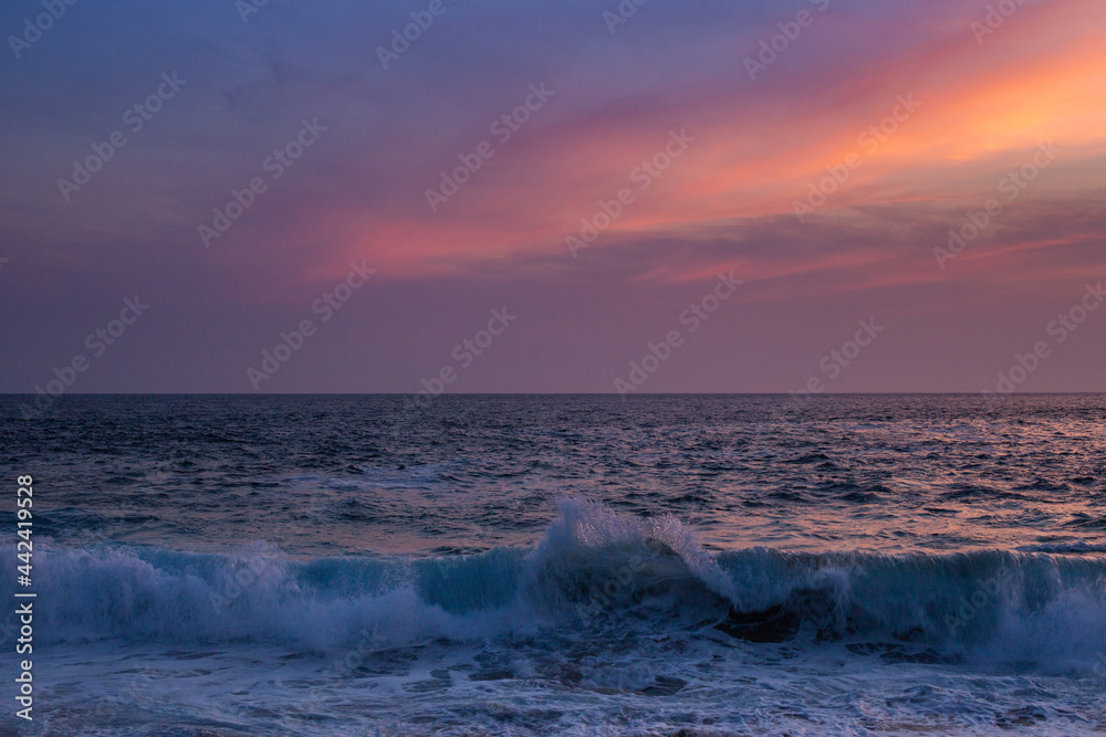 colorful sunset on a beach in summer. a wave breaks close to the sand.