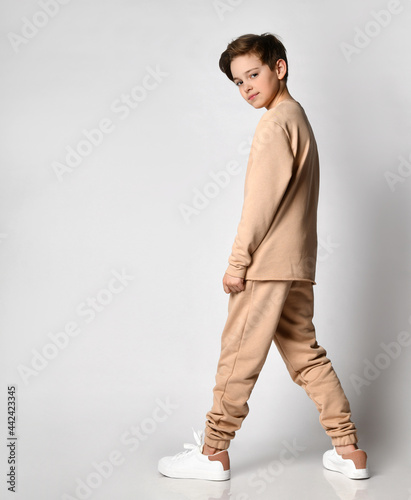 stylish teenager is half-turned and looks from the underhead, he is dressed in a comfortable beige cotton suit photo