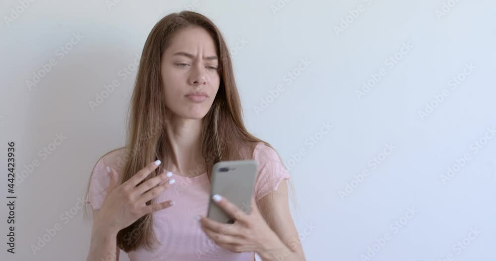 Attractive young woman making selfie photo on smartphone over white background, posing, making face, dissatisfied with photo at first, then female liked photo, smile, shine with happiness. copy space Attractive young woman making selfie photo on smartphone over white background, posing, making face, dissatisfied with photo at first, then female liked photo, smile, shine with happiness. copy space