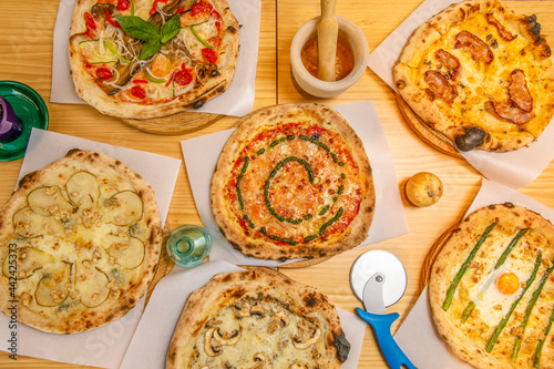 Top view image of delicious and original pizzas with pear, mushrooms, pesto sauce, green asparagus and fried eggs on pine wood table