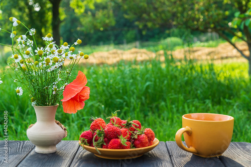 Summer still life of a plate with strawberries and coffee on a table with flowers. Summer morning or evening background