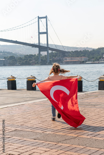 Girl hold Turkish flag near Bosphorus bridge  aka15 July Martyrs Bridge or 15 Temmuz Sehitler Koprusu  in Ortakoy  Istanbul  Turkey. Patriotism. Turkish National Sovereignty and and Children s day.