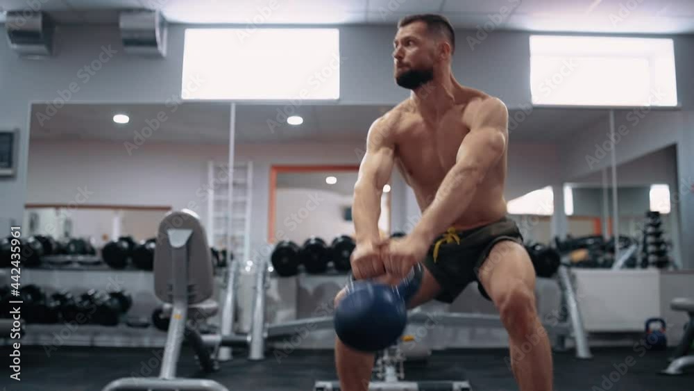 The young man, with a bare chest, performs a dumbbell exercise in the gym. Intense masculine energy. Healthy lifestyle. Sport concept The young man, with a bare chest, performs a dumbbell exercise in the gym. Intense masculine energy. Healthy lifestyle. Sport concept