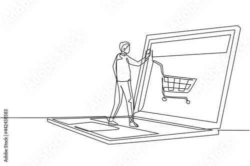 Single continuous line drawing young male shopping online via giant laptop screen with shopping cart inside. Sale, digital lifestyle concept. Dynamic one line draw graphic design vector illustration