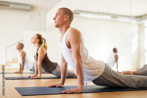 Nice people exercising during yoga class in modern fitness center