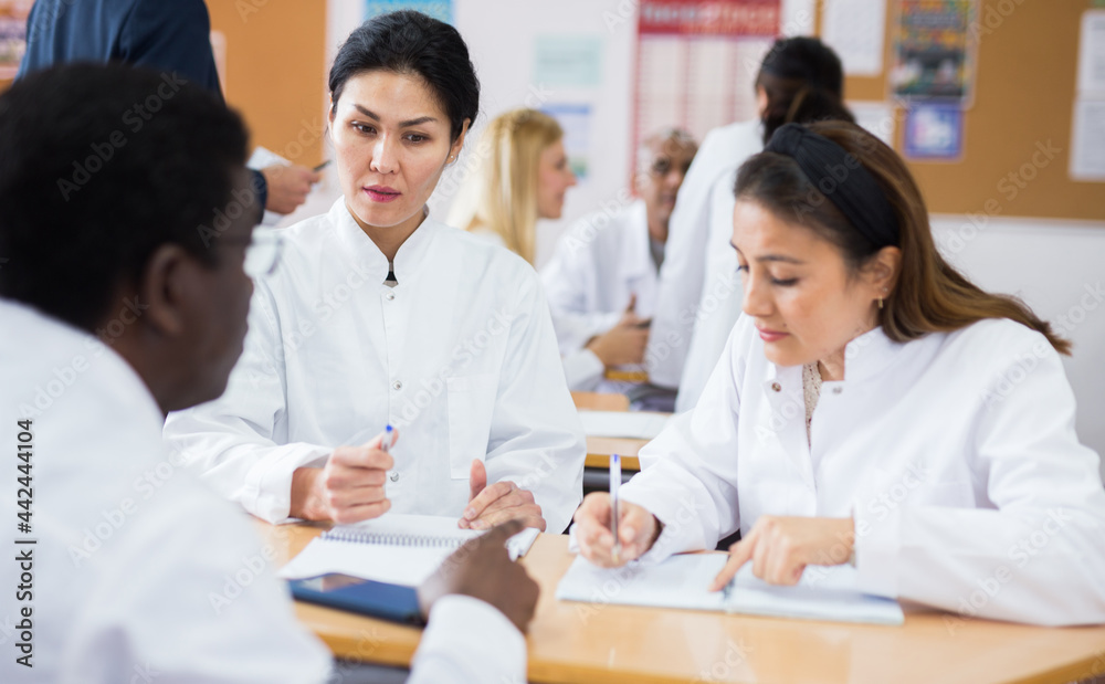 Obraz premium Positive men and women in white medicine coats working in groups during lesson
