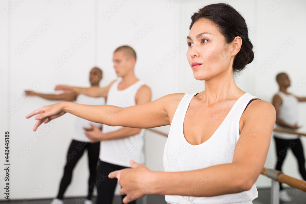 Asian girl in leotard training in ballet class with other dancers