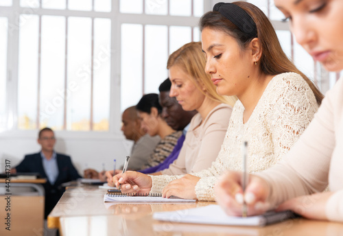 Portrait of focused young adult female sitting at desk studying in classroom with colleagues