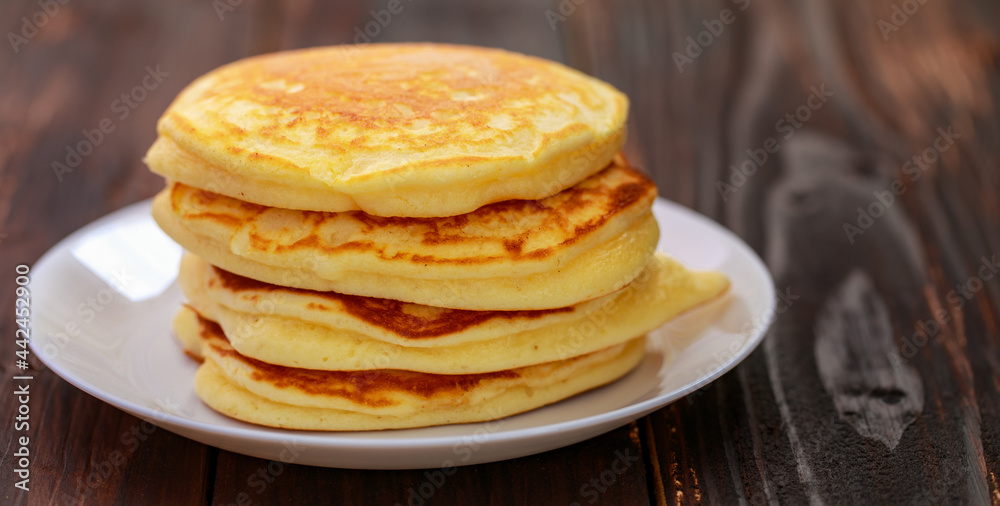 Stack of delicious pancakes in white plate on brown wooden background. It is a homemade breakfast Thick, soft, scented with butter.