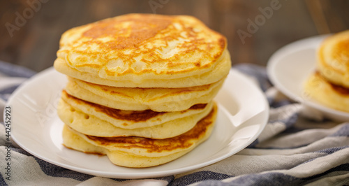 Stack of delicious pancakes sweet food on plaid fabric in white plate on wooden background.