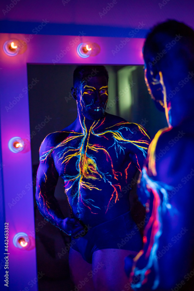 UV patterns body art of the circulatory system on a man's body. On the torso of a muscular athlete, veins and arteries are drawn with fluorescent dyes. Bodybuilder standing by the mirror with lamps. UV patterns body art of the circulatory system on a man's body. On the torso of a muscular athlete, veins and arteries are drawn with fluorescent dyes. Bodybuilder standing by the mirror with lamps.