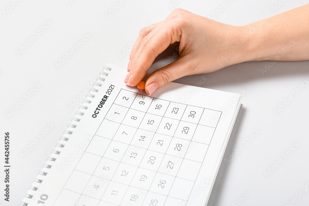 Woman marking date in calendar on light background, closeup Woman marking date in calendar on light background, closeup