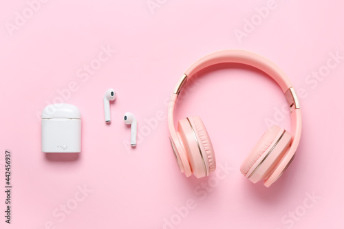 Modern headphones and earphones on color background