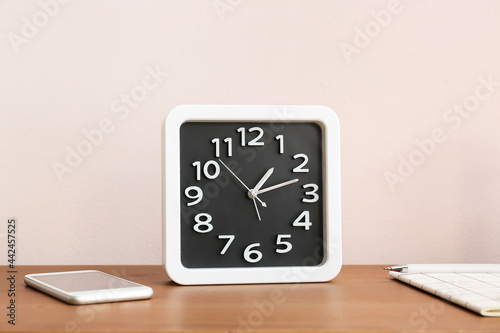 Stylish clock and mobile phone on table near light wall