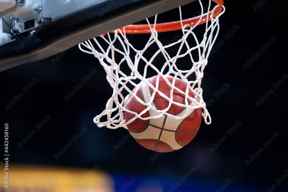 The orange basketball ball flies through the basket. Professional sport concept..
