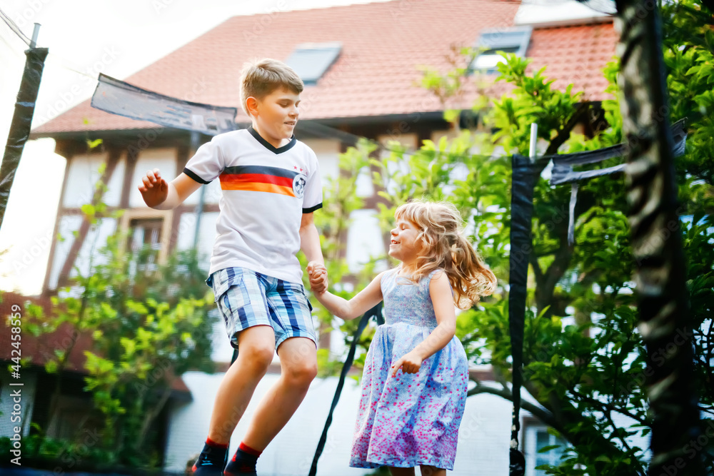 Fototapeta premium Little preschool girl and school kid boy jumping on trampoline. Happy funny siblings children having fun with outdoor activity in summer. Sports and exercises for kids. Family have fun.