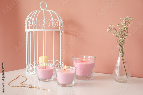 Burning candles and decor on shelf near color wall