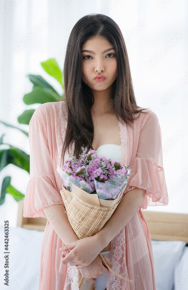 Beautiful young naughty sexy girl on white underwear and pink pajamas stand on knees on white bed happily holding bunch of purple flower as romantic gift for special day Beautiful young naughty sexy girl on white underwear and pink pajamas stand on knees on white bed happily holding bunch of purple flower as romantic gift for special day
