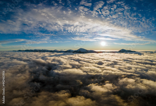 Aerial view of vibrant sunrise over white dense fog with distant dark Carpathian mountains on horizon.
