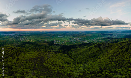 Aerial wide panoramic view of dark mountain hills covered with green mixed pine and lush forest in evening.