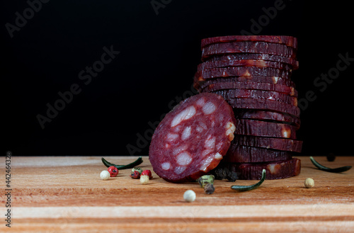 Dry sausage with spiceson wooden board and black background photo