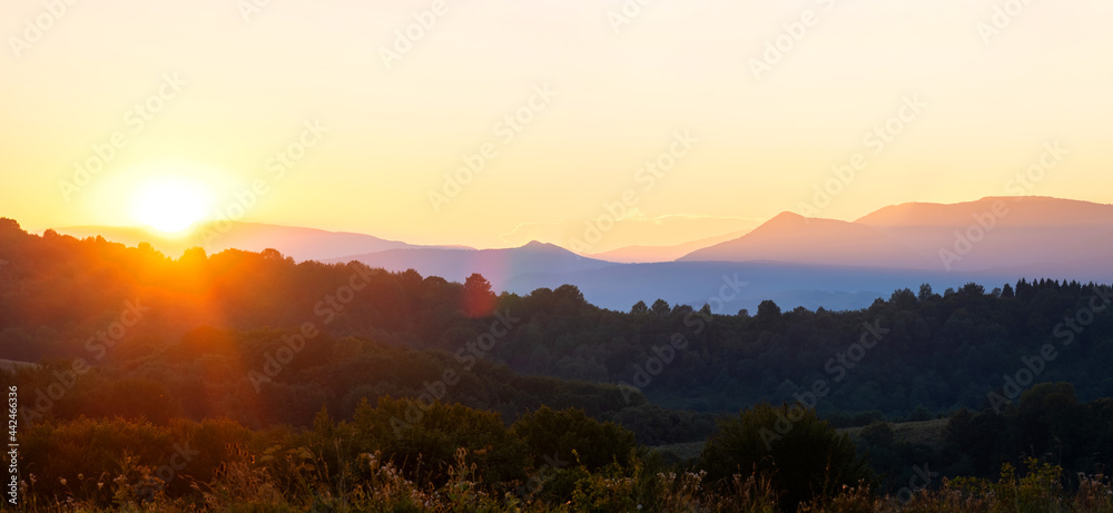 Beautiful panoramic mountain landscape with hazy peaks and foggy valley at sunset.